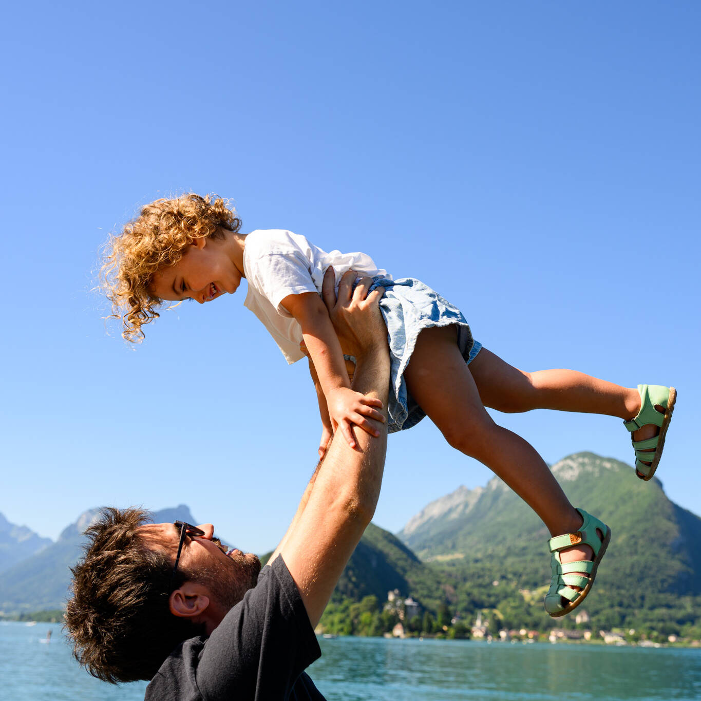 Père soulevant sa fille ciel bord lac Annecy Talloires séance photo famille photographe